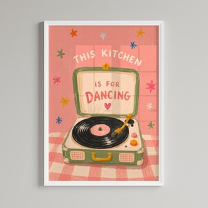May include: A framed art print featuring a vintage-style record player with the text "THIS KITCHEN IS FOR DANCING." The artwork has a pink and green color scheme with star and heart accents, set against a checkered background.