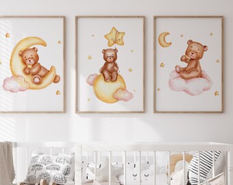 May include: Three watercolour prints featuring a brown teddy bear on a yellow moon, a yellow moon with clouds, and a pink cloud with stars. The prints are framed in a light wood frame.