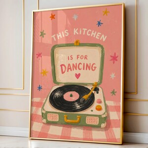 May include: A framed art print featuring a vintage-style record player with the text "THIS KITCHEN IS FOR DANCING." The artwork has a pink background with colorful star accents and a pink and white checkered pattern.
