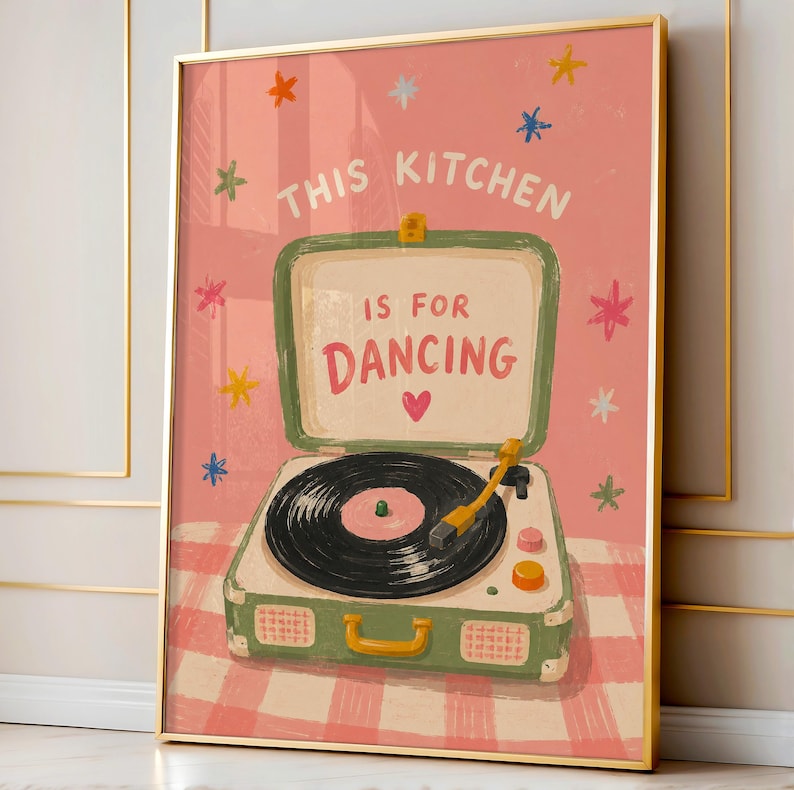 May include: A framed art print featuring a vintage-style record player with the text "THIS KITCHEN IS FOR DANCING." The artwork has a pink background with colorful star accents and a pink and white checkered pattern.