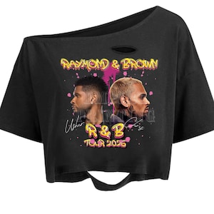 May include: Black crop top with a distressed neckline and hem. The shirt features a graphic of two men's faces and the text "RAYMOND & BROWN" in yellow and pink, along with "R&B TOUR 2026".