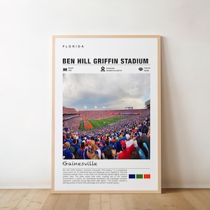 May include: A framed poster featuring Ben Hill Griffin Stadium in Gainesville, Florida. The image shows a packed stadium with a green field and red seating. Text includes "Florida", "Ben Hill Griffin Stadium", and "Gainesville".