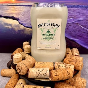 May include: A bottle of Appleton Estate Signature Jamaica Rum, surrounded by corks. The label features the brand name and the words "Signature Jamaica Rum." The background shows a beach scene with a sunset.