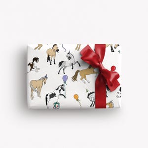 May include: A wrapped gift with white paper featuring a pattern of cartoon horses in various colours and poses, some with party hats and balloons. A large red satin bow adorns the top of the package, adding a festive touch.