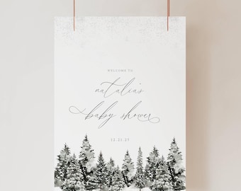 Könnte beinhalten: Ein weißes Babyparty-Schild mit dem Text "Welcome to Natalia's baby shower" in eleganter Schrift. Der untere Teil des Schildes zeigt eine Aquarellillustration von schneebedeckten Kiefern. Das Datum 12.21.25 ist ebenfalls enthalten.