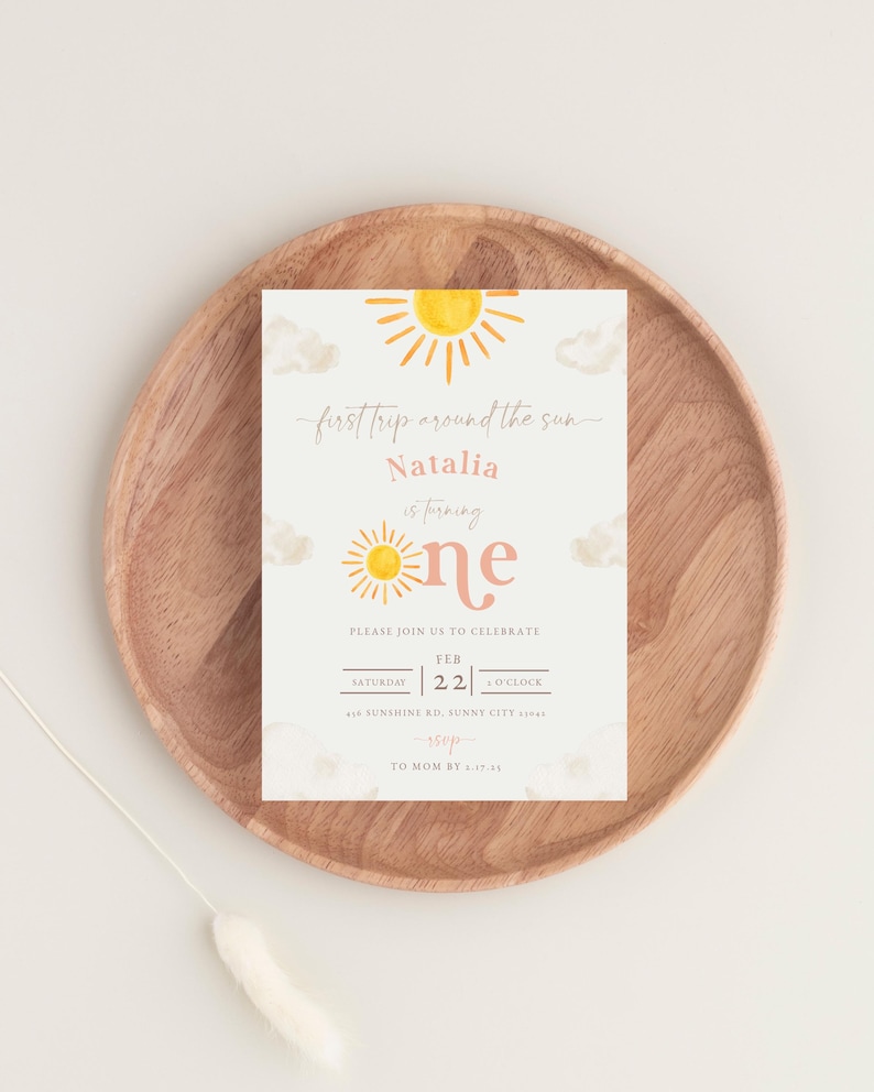 May include: A yellow and orange sun with a pink "one" on a white background with clouds. The text "first trip around the sun" and "Natalia is turning" is written in cursive. The invitation is for a first birthday party on 22nd February at 4 o'clock. The address is 456 Sunshine Rd, Sunny City 51005. RSVP by 27th April.