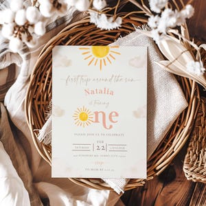 May include: A light blue invitation with a yellow sun and clouds. The text reads "first trip around the sun Natalia is turning one" with a pink number one. The invitation also includes details for a party on 22nd February at 1 o'clock.