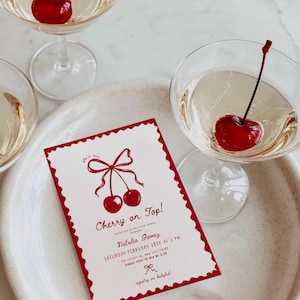 May include: A rectangular invitation card with a scalloped red border, featuring a red illustration of two cherries tied with a bow. The text reads: she's our Cherry on Top! Please join us for a baby shower honouring Natalia Gomez, Saturday February 28th at 3 PM, 214 Cherry Ln, Bow City 29408, kindly RSVP to Mia by 2.20, registry on babylist.