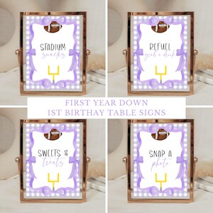 May include: Four printable table signs for a football-themed first birthday party. Each sign features a purple and white gingham background with a football and a football goal post. The signs read "Stadium Snacks", "Refuel Grab a Drink", "Sweets & Treats", and "Snap a Photo".