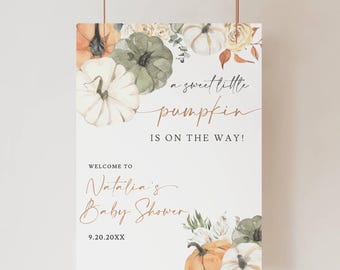 May include: A rectangular baby shower sign with a watercolor design. The sign features pumpkins in shades of orange, white, and green, along with floral accents. Text reads "a sweet little pumpkin is on the way!" and "Welcome to Natalia's Baby Shower."