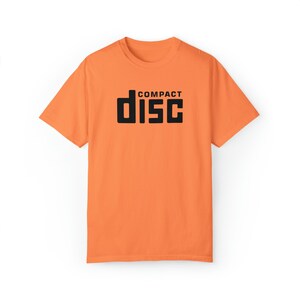 Może przedstawiać: Pomarańczowy T-shirt z czarnym napisem "COMPACT DISC" w retro czcionce.