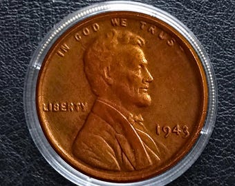 May include: A copper-coloured 1943 Lincoln penny, in a clear plastic holder. The coin shows a profile of Abraham Lincoln, with the words "LIBERTY" and "IN GOD WE TRUST". The year "1943" is also displayed on the coin.