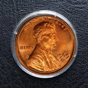 May include: A copper-colored 1969 S Lincoln penny encased in a clear plastic holder. The coin features a profile of Abraham Lincoln, the word "LIBERTY", and the phrase "IN GOD WE TRUST".
