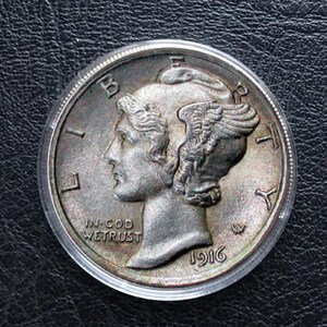 Könnte beinhalten: Nahaufnahme einer silbernen Mercury-Dime von 1916, die das Profil einer Frau mit geflügelten Haaren zeigt. Die Münze ist in einem transparenten Kunststoffhalter eingeschlossen. Die Worte "IN GOD WE TRUST" sind sichtbar.