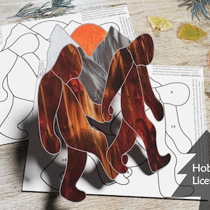 May include: A stained glass craft kit featuring two figures walking with a mountain and sun behind them. The figures are made of stained glass pieces in shades of orange, red, and brown. The kit includes a pattern sheet and instructions for assembling the stained glass figures.