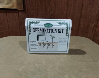 May include: A white box labeled "GERMINATION KIT" with text and illustrations of the germination process. The box includes the text "FROM OUR FARM MAYERS TO YOUR HOME". The kit contains seeds, a seed starter, a viewing stand, instructions, and experiments.