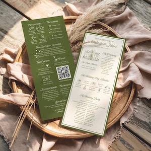 May include: Two wedding invitation cards with green borders and text, one with wedding details and the other with fun facts. The cards are on a wooden tray with dried plants. The text includes the wedding date, names, and venue.