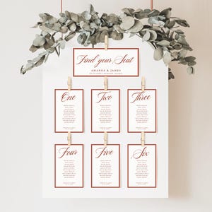 Könnte beinhalten: Ein weißes Hochzeitssitzplan-Schild mit der Überschrift Find your Seat, Amanda & James, 09.09.202X. Sechs rechteckige Karten, beschriftet von One bis Six, sind mit Holzklammern befestigt und listen Namen in einer dunkelroten Schrift auf.