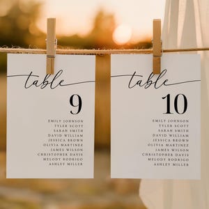 May include: Two white table number cards, labeled "table 9" and "table 10", are suspended by wooden clothespins. Each card features a list of names below the number, with a blurred background.