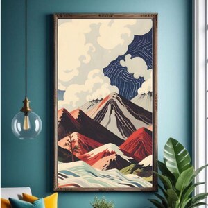 Puede incluir: Una impresión enmarcada de un paisaje de montaña. La obra de arte presenta montañas estilizadas en tonos rojos, grises y negros, con nubes blancas y un cielo azul. La impresión se exhibe en una habitación con una pared verde azulado y una silla de madera.