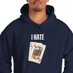 Puede incluir: Una sudadera con capucha azul marino con el texto "I HATE" impreso en blanco en la parte delantera. Una carta de juego con el Jack of Hearts está impresa debajo del texto.