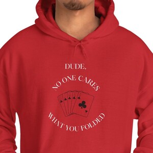Puede incluir: Sudadera con capucha roja con texto blanco que dice "DUDE, NO ONE CARES WHAT YOU FOLDED" y un gráfico de cartas de juego.