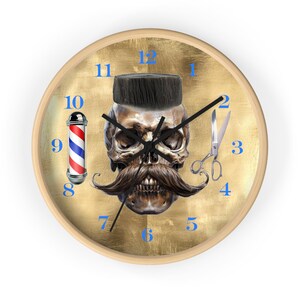 May include: A round wall clock with a light wood frame. The clock face features a skull with a dark mustache and a dark, flat-top hairstyle. Blue numbers mark the hours, and a barber pole and scissors are also depicted.