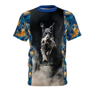 Peut inclure: T-shirt à manches courtes avec une image dynamique d'un chien noir courant avec un petit animal dans la gueule. Le t-shirt a un col bleu et des motifs abstraits colorés sur les manches et les côtés.