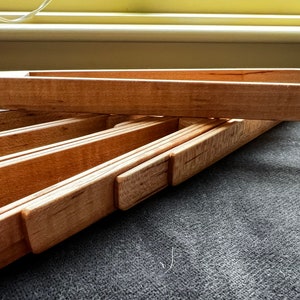 Puede incluir: Un juego de pinzas de madera, plegadas juntas, con un acabado de madera natural. Las pinzas están hechas de varias piezas de madera, unidas para crear una herramienta resistente y funcional.