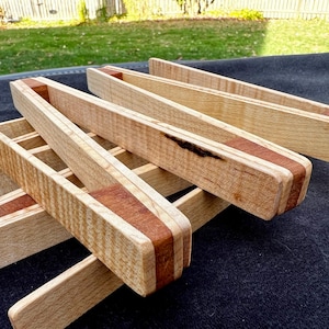 Puede incluir: Conjunto de cinco tenazas de madera con un acabado de madera natural y un acento rojo-marrón. Las tenazas están hechas de madera de arce y tienen un patrón de veta único.