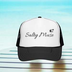 Może przedstawiać: Czarno-biała czapka typu trucker z napisem "Salty Muse" w ozdobnej czcionce oraz grafiką fali i palmy. Czapka ma czarny daszek i siatkową tylną część, idealna na plażę lub do noszenia na co dzień.