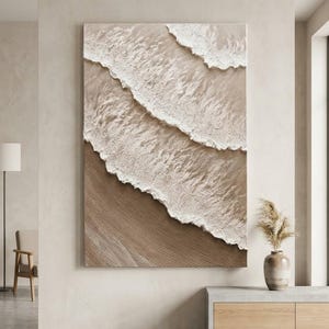 Könnte beinhalten: Ein großes, rechteckiges Wandbild mit einer strukturierten, dreidimensionalen Darstellung von Meereswellen, die auf einen Sandstrand treffen. Das Kunstwerk verwendet eine neutrale Farbpalette aus Beige, Hellbraun und Weiß mit sichtbaren Reliefs.