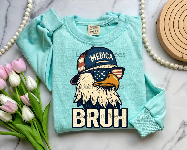 以下が含まれることがあります： サングラスと「'Merica」の文字が入った帽子をかぶった漫画のワシが描かれた、水色の長袖シャツ。「BRUH」の文字が下にプリントされています。このシャツはクルーネックで、袖口はリブ編みです。