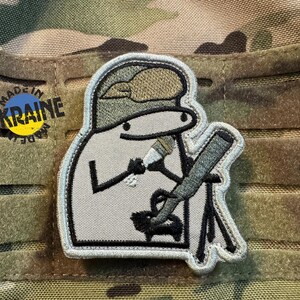 Oekraïense geborduurde moraalpatch met een cartoonachtige mortiergranaat die een mortier laadt. Klittenbandsluiting. 8 x 7 cm. Originele humoristische militaire patch.