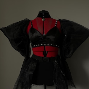 May include: A black satin crop top with a heart-shaped pendant necklace and a black tulle skirt with a chain belt. The top has a beaded trim and the skirt has a layered design.