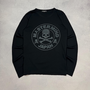 May include: Black long-sleeve shirt with a crew neck. The shirt features a gray circular graphic on the front with a skull and crossbones design, and the words "MASTERMIND JAPAN" in a circular pattern around the skull.