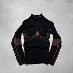 May include: Black athletic long-sleeved top with a high neck. The shirt features orange detailing on the sleeves and chest. The brand name "BIONIC" is printed on the collar.