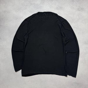 以下が含まれることがあります： 黒色の長袖Tシャツ、クルーネック。 シャツは柔らかく軽量な素材で作られています。 衣類は灰色の表面に平らに置かれています。
