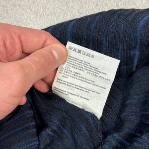 Puede incluir: Primer plano de una prenda de tejido acanalado azul marino con rayas azul oscuro. Se muestra una etiqueta blanca con instrucciones de cuidado, incluyendo lavado a mano y secado en plano.