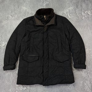 May include: A black quilted jacket with a brown fur-lined collar and two front pockets. The jacket has a button and zipper closure. The sleeves are cuffed at the wrists. The jacket is a medium length.