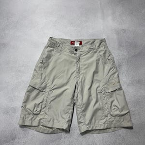 以下が含まれることがあります： ベージュ色のカーゴショーツ。複数のポケットとボタン留めが付いています。 ショーツはゆったりとしたフィット感で、ウエストバンドの近くに小さなタグが付いています。 軽量素材で作られています。