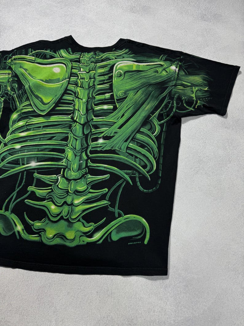 Puede incluir: Camiseta negra con un dise&ntilde;o de esqueleto verde vibrante. El gr&aacute;fico incluye detalles de la caja tor&aacute;cica, la columna vertebral y los om&oacute;platos, creando un efecto visual impactante. El dise&ntilde;o est&aacute; impreso sobre un fondo negro.