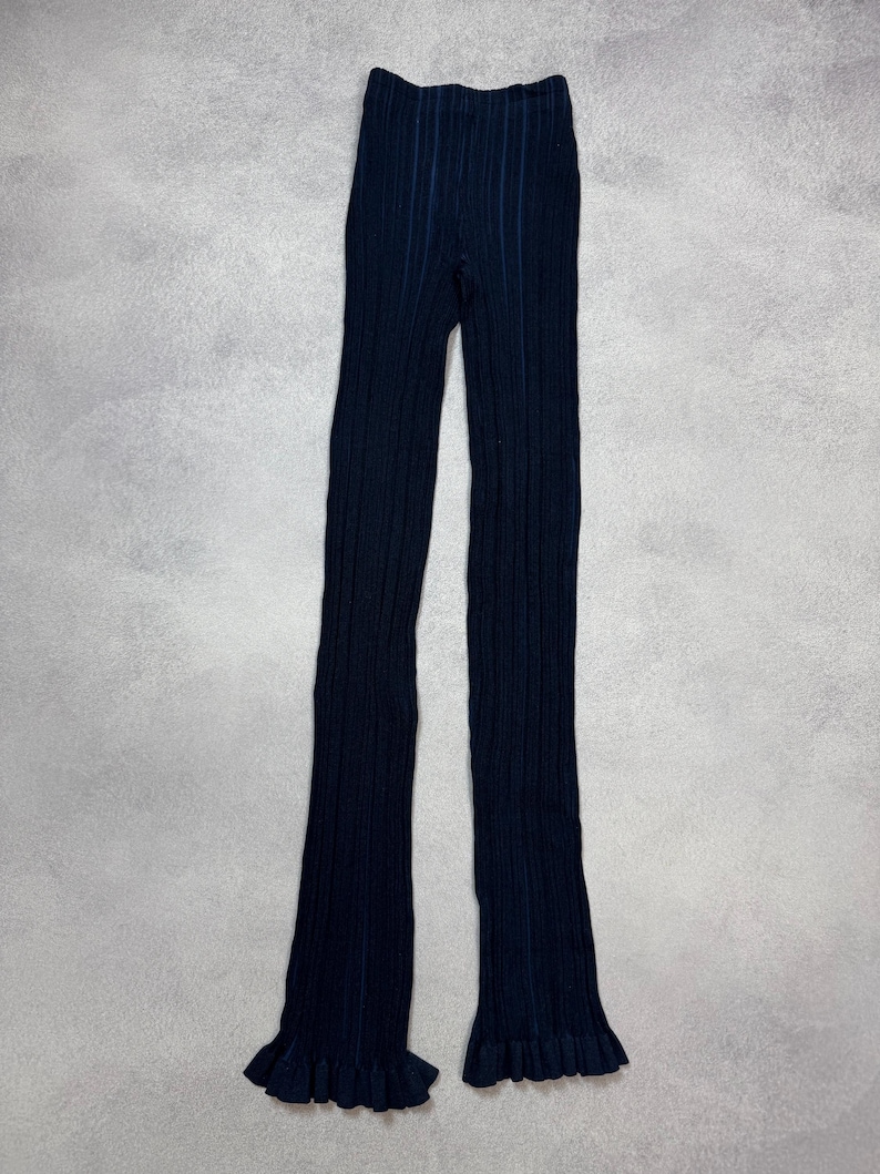 Puede incluir: Pantalones de punto acanalado azul marino con dobladillo con volantes. Los pantalones tienen un dise&ntilde;o acanalado vertical y una silueta ajustada. La tela parece ser un material de punto suave.