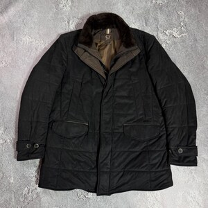 May include: A black quilted jacket with a brown fur collar. The jacket has two front pockets and buttoned cuffs. The jacket has a brown interior lining and a small logo on the chest.