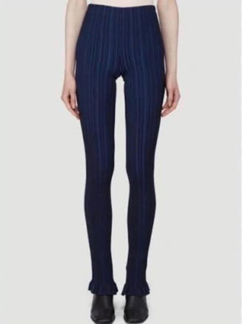 Puede incluir: Leggings azul marino con rayas verticales, cintura alta y dobladillos con volantes. Los leggings son ajustados y parecen estar hechos de una tela acanalada. El modelo lleva zapatos negros.
