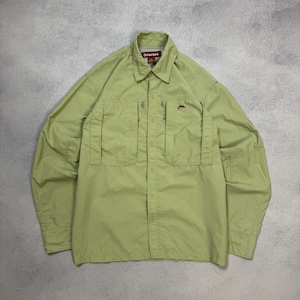May include: A light green button-down shirt with two chest pockets and a collar. The shirt has the brand name "SIMMS" on a tag and a small red fish logo. The long-sleeved shirt is made of a lightweight material.