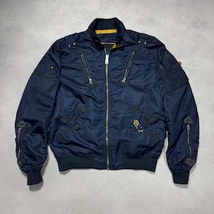 Könnte beinhalten: Marineblaue Bomberjacke mit mehreren Reißverschlusstaschen und geripptem Kragen und Bündchen. Die Jacke hat ein gelbes Innenfutter und kleine Aufnäher auf den Ärmeln. Ein klassisches, stilvolles Oberbekleidungsstück.