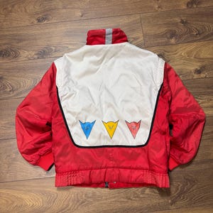 May include: A red and white vintage jacket with a stand-up collar and a zipper closure. The back features a white panel with three colored triangle logos: blue, yellow, and red. The jacket has red cuffs and a gray stripe on the collar.
