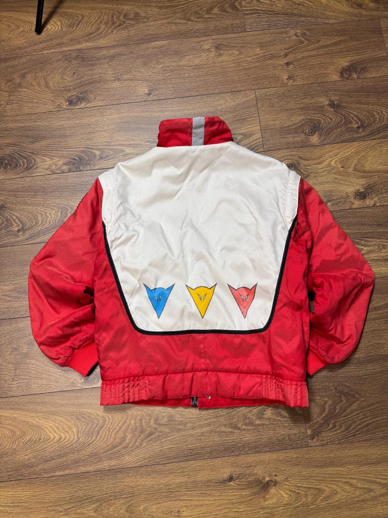 May include: A red and white vintage jacket with a stand-up collar and a zipper closure. The back features a white panel with three colored triangle logos: blue, yellow, and red. The jacket has red cuffs and a gray stripe on the collar.