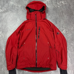 May include: A red hooded jacket with a black zip and black detailing. The jacket features a Mammut logo on the sleeve and multiple pockets. It has a hood and black cuffs.
